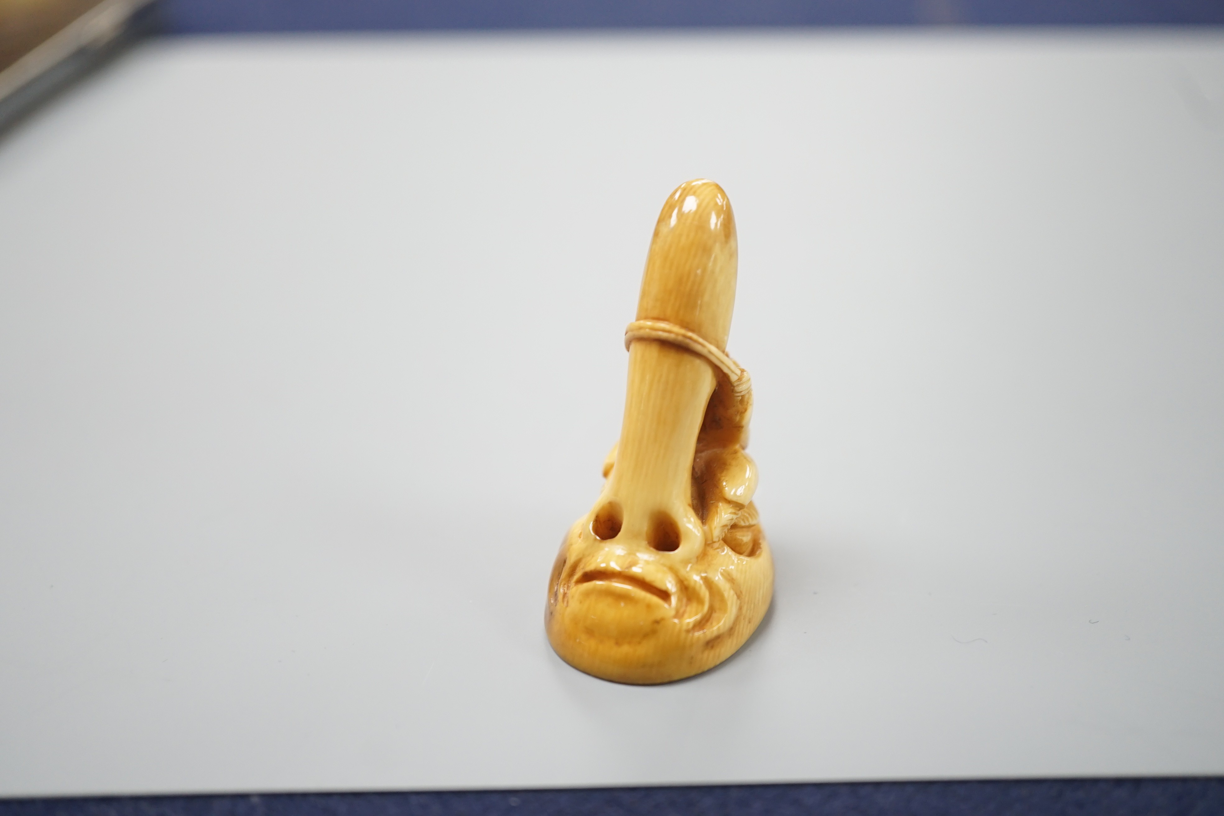 A Japanese ivory netsuke of a man climbing a giant Tengu noh mask, 19th century, 4.2cm